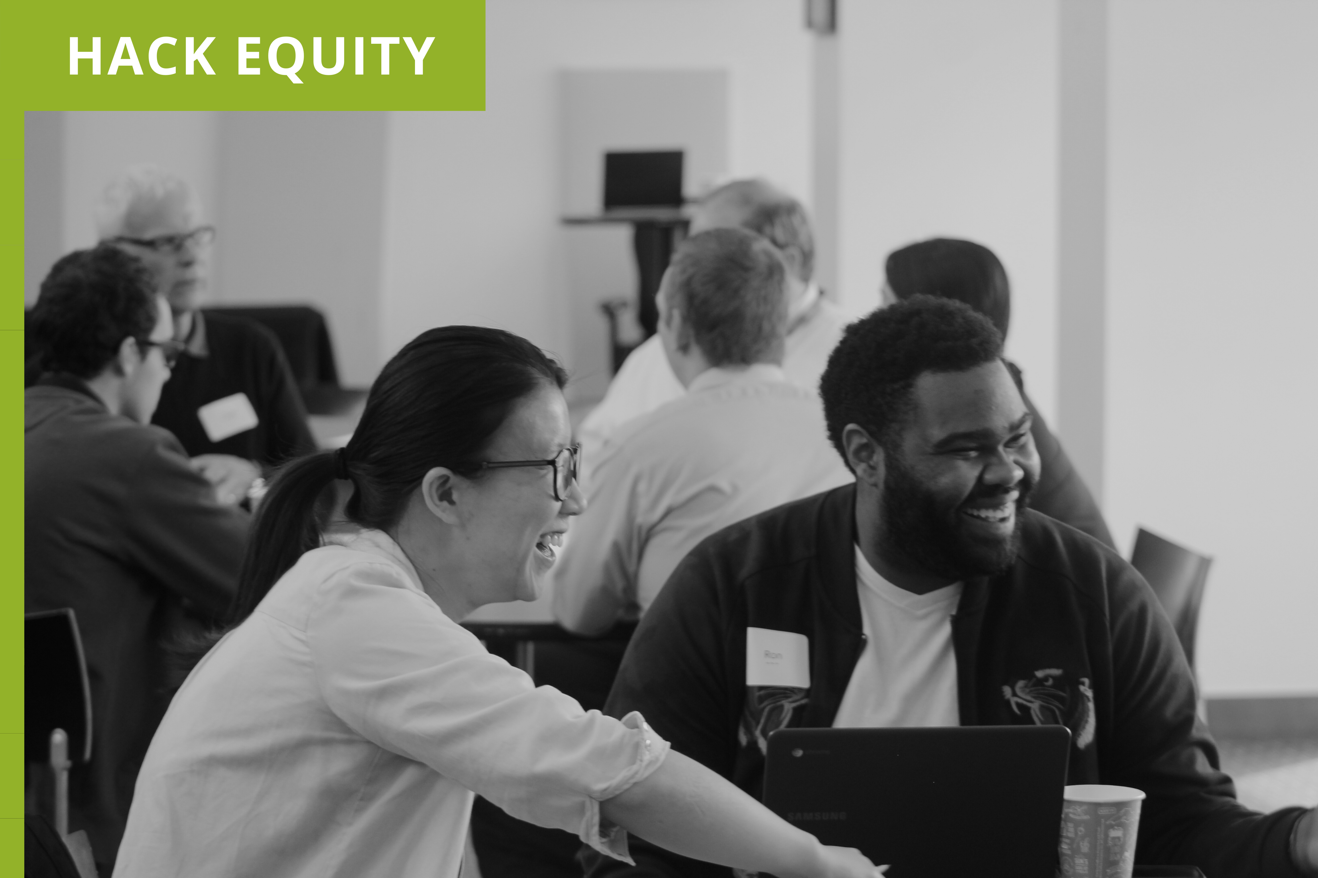 A diverse team smiling and laughing while collaborating on their project at our design thinking workshops. Green label in the left corner with the project title, Hack Equity.