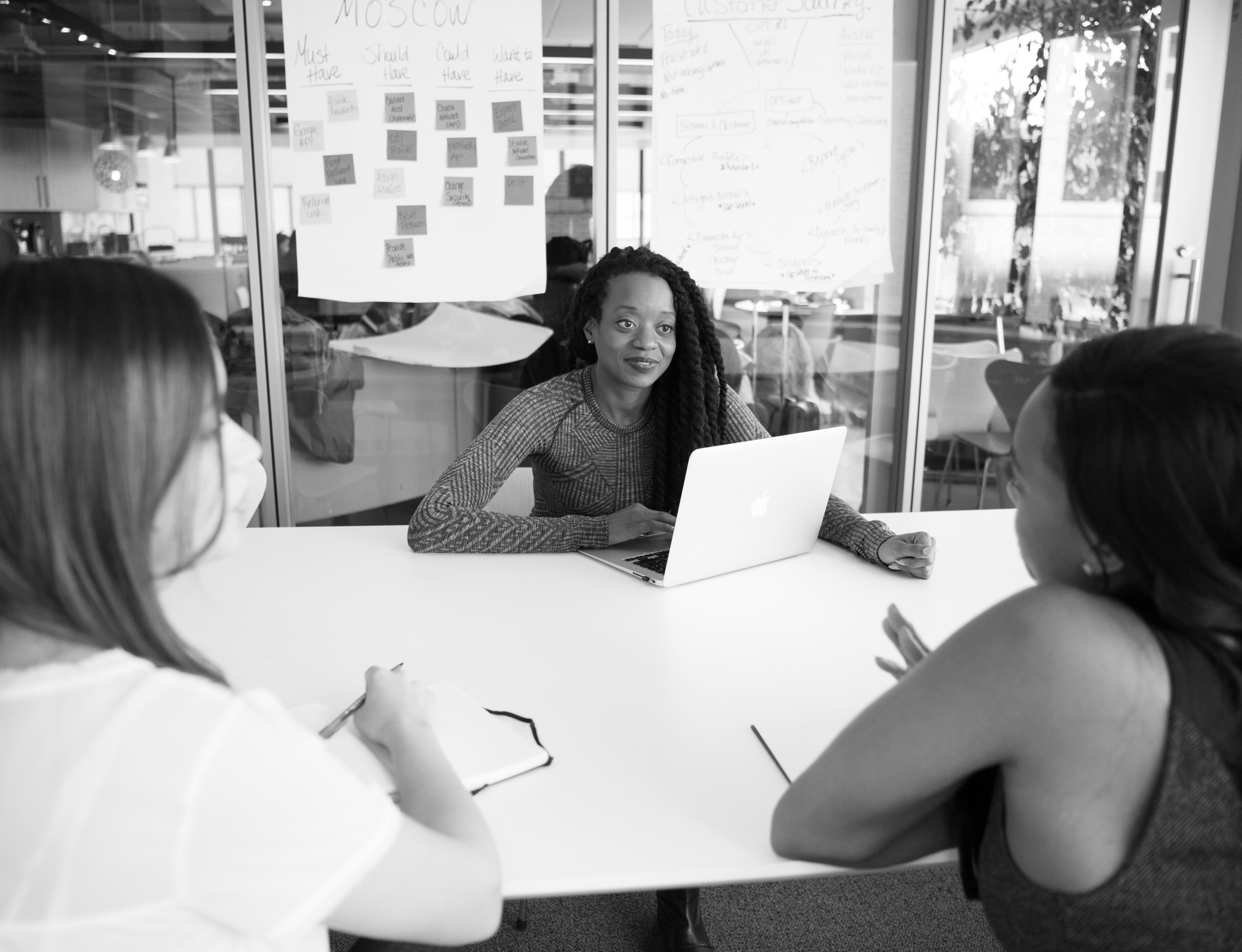 A diverse group of woman with notepads and a laptop collaborating on a project.