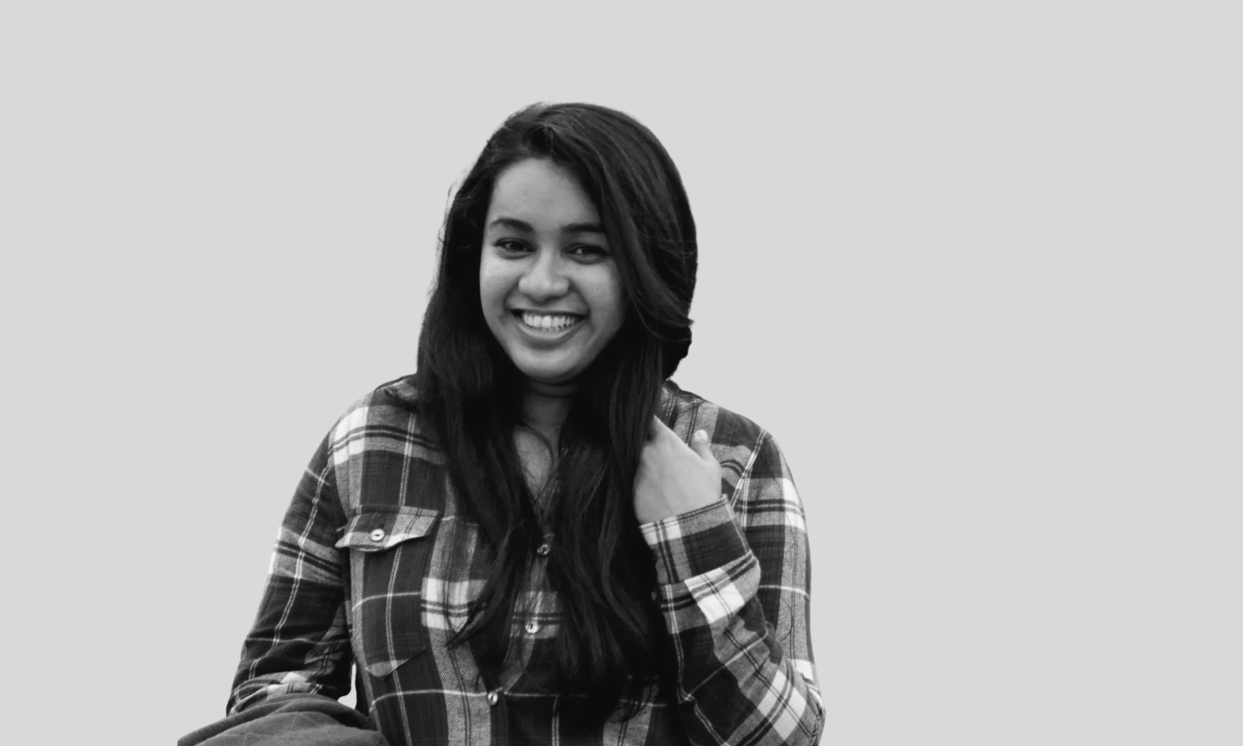 An Asian woman looks at the camera and smiles widely. She has long, straight black hair and is wearing a button-down plaid shirt.