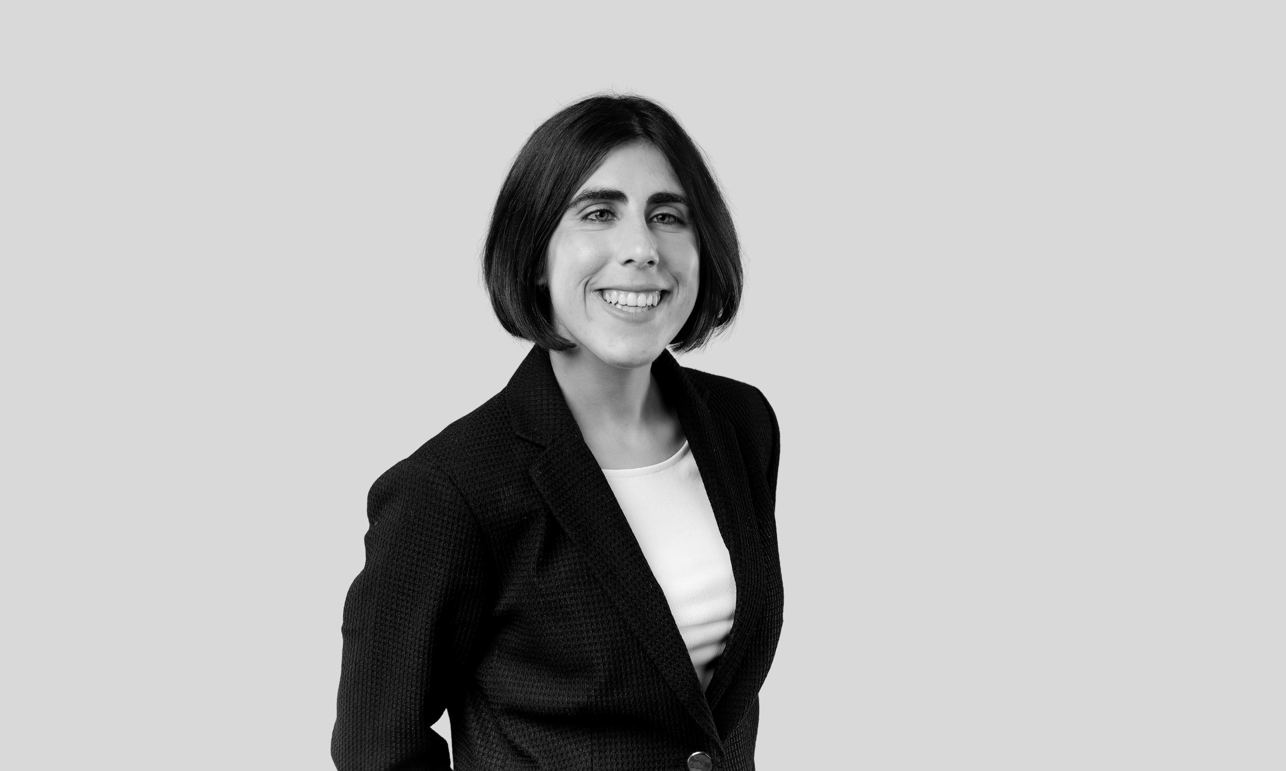 A white woman faces askew from the camera and smiles. She has straight black hair styled in a bob and is wearing a black blazer and a white shirt.